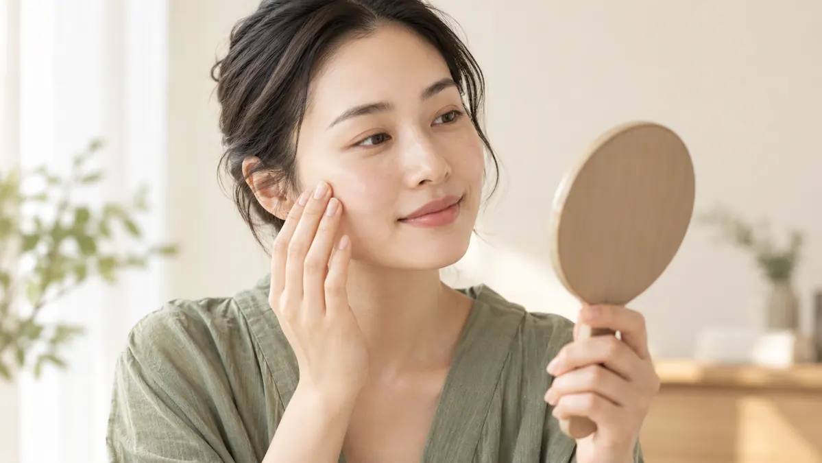 Woman holding a hand mirror and checking the skin on her cheek